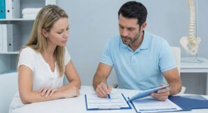 A patient and a chiropractor reviewing medical forms and insurance paperwork together at a desk, ensuring proper documentation of injuries.